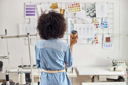 African-American woman fashion designer near sewing machines in workshop backside view