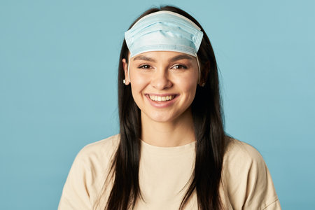 Smiling pretty lady standing in a disposable protective mask from viruses on the foreheadの写真素材