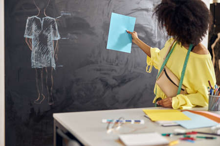 African-American teacher shows blank blue paper against blackboard at sewing classの写真素材