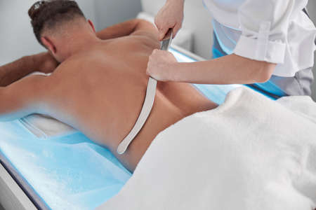 Therapist uses gua sha tool to massage back of patient in contemporary clinic officeの写真素材