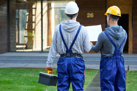 Plan it. Rear view of two builders standing outdoors with an open blueprint discussing the interior of a half completed cottage houseの写真素材