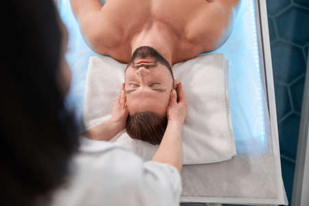 Relaxed man with beard lies on couch undergoes massage procedure in clinic