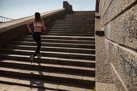 Woman in tracksuit runs up stone steps on city embankment on sunny dayの写真素材