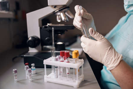 Laboratorian in latex gloves takes liquid from test tube to research material at workplaceの写真素材