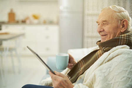 Smiling male pensioner using tablet to communicate with doctorの写真素材