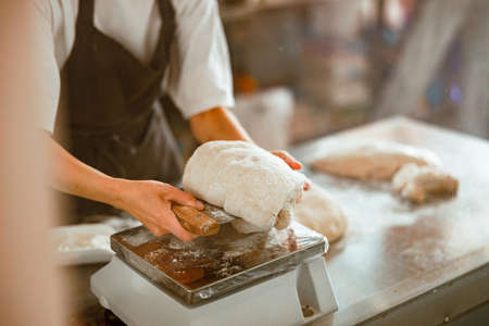 Woman cuts piece of fresh raw dough in contemporary craft bakery shopの写真素材