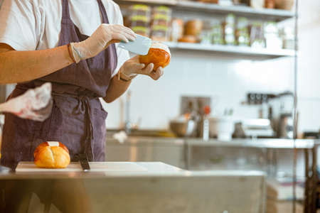 Confectioner plains delicious cream inside fresh bun in craft bakery shopの写真素材