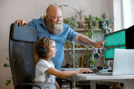 Positive bearded man teaches daughter to work with computer program at workplaceの写真素材