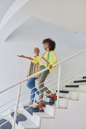 African-American dressmaker points on something in front to mature colleague going down on stepsの写真素材