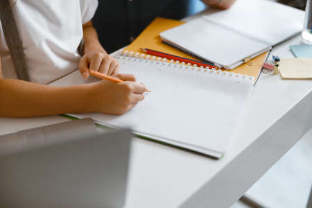 Little girl draws in copybook with yellow pencil doing homework at table in roomの写真素材
