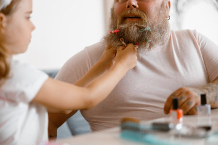 Girl puts colorful scrunchie onto long father beard playing together at homeの写真素材
