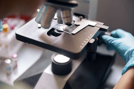 Woman lab assistant adjusts microscope with sample on slide in laboratory closeupの写真素材