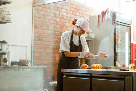 Smiling woman pours powdered sugar onto fresh buns at table in craft bakery shopの写真素材