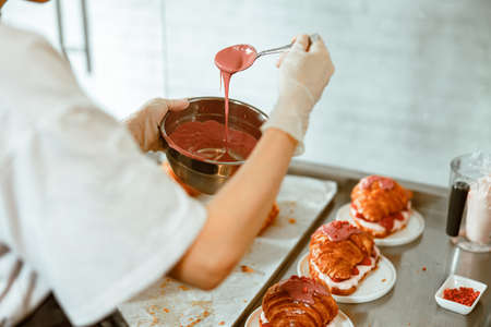 Confectioner holds sticky pink frosting at table with delicious croissants in bakeryの写真素材