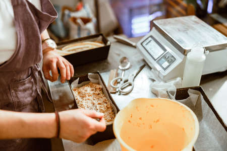 Employee spreads raw dough in dish with fork at metal table