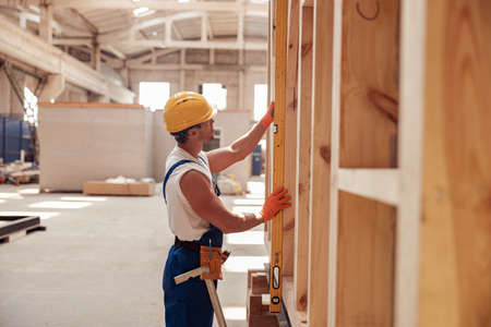 Male builder measuring wood siding of construction cabin