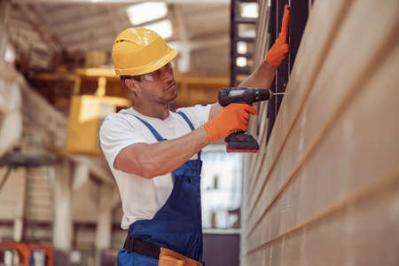 Handsome male worker using power drill at construction site