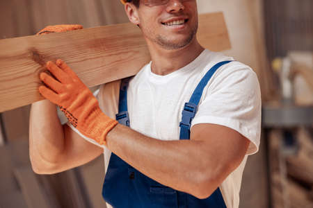 Joyful worker carrying timber wood plank at construction siteの写真素材