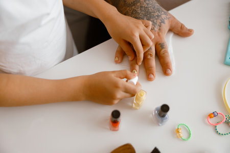Little girl applies yellow polish onto daddy nails at white table in roomの写真素材