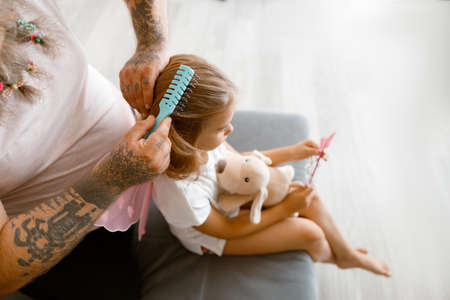 Man with scrunchies in beard brushes girl hair in living roomの写真素材
