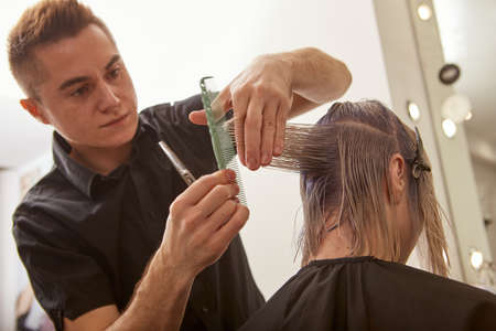 Handsome hairdresser cutting woman hair with professional scissorsの写真素材