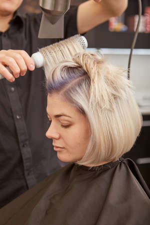 Hairdresser styling young woman hair in beauty salonの写真素材