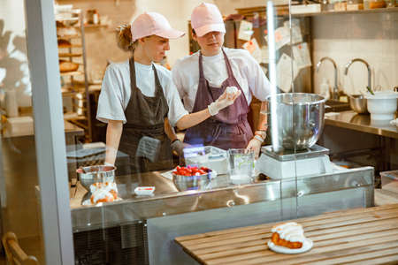 Lady gives chicken egg to colleague making dough at table in bakeryの写真素材