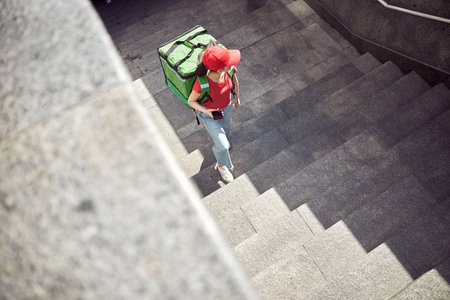 Asian delivery lady walking down urban streetの写真素材