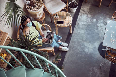 Asian woman in protective mask sit indoors with laptopの写真素材