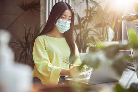 Young lady in protective face mask studying in cafeの写真素材