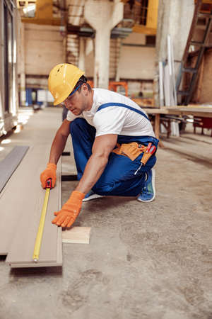 Male builder measuring timber plank at construction site