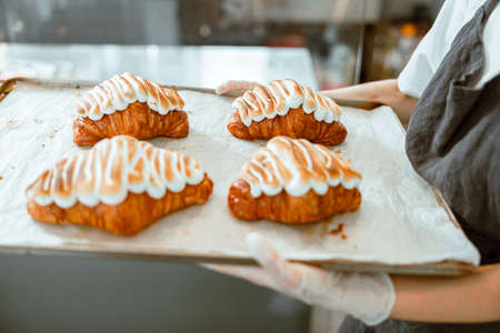 Employee in gloves holds delicious croissants in craft bakery shopの写真素材