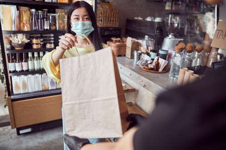 Woman in mask taking order from waitress at cafeの写真素材