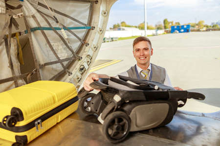 Cheerful man airline worker putting travel suitcase in aircraftの写真素材