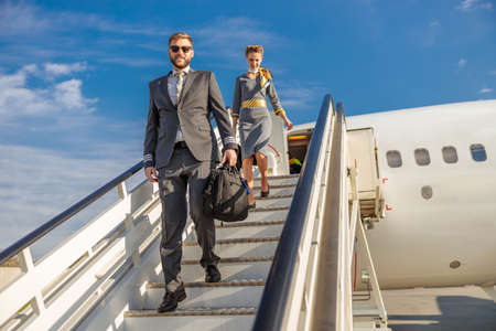 Smiling pilot and stewardess walking down airplane stairs