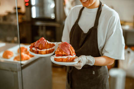 Worker in uniform holds tasty croissants with filling in craft bakery shop closeupの写真素材