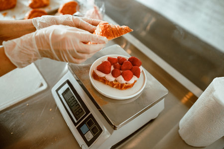 Skilled confectioner puts top onto croissant with juicy strawberries and cream in craft bakeryの写真素材