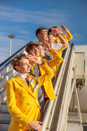 Cheerful airline workers standing on airplane stairs under blue skyの写真素材
