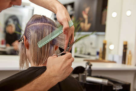Hairdresser hands cutting woman hair with professional scissorsの写真素材