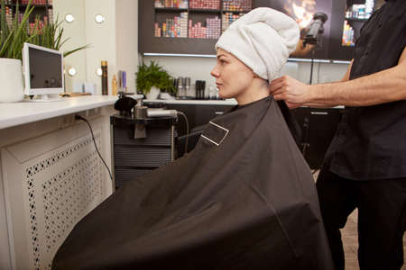 Hairdresser putting hairdressing cape on client in beauty salonの写真素材