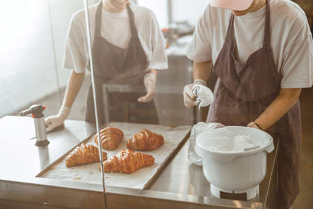 Worker fills confectioner with delicious cream at table with croissants in craft bakery shopの写真素材