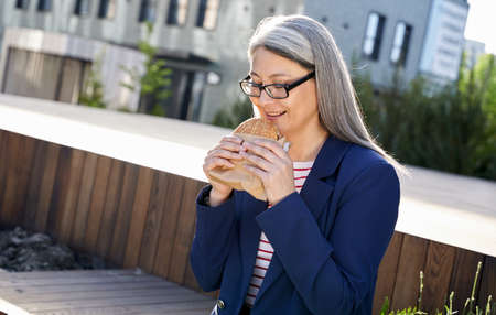 Successful experienced business lady savouring her burger on sunlit terrace