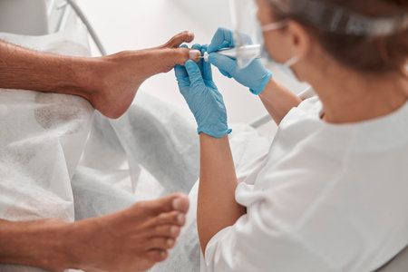 Woman master polishes toenail of male client with tool at procedure in beauty salonの写真素材