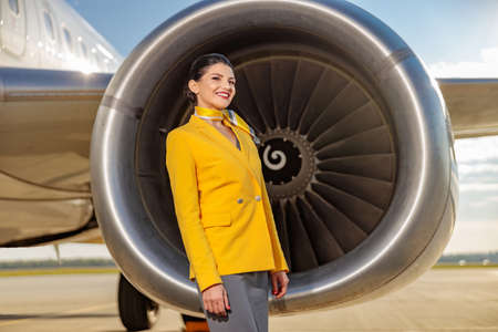 Cheerful woman stewardess standing near aircraft engineの写真素材