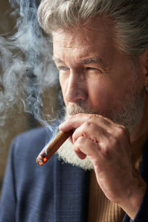 Close up portrait of brutal grey haired mature man looking away while smoking cigarの写真素材