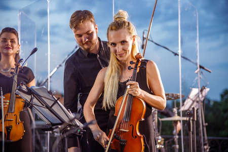 Beautiful woman violin player playing in orchestra outdoors