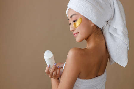 Asian young woman with patches under eyes holding deodorantの写真素材