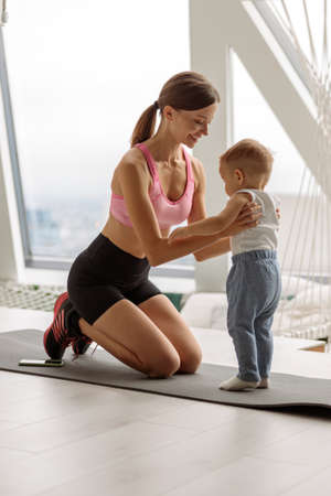 Mom and her baby on a sports mat in the roomの写真素材
