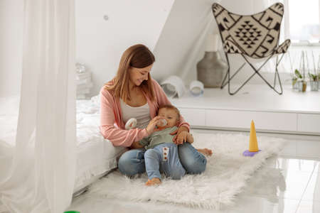 Little baby boy drinking juice from a bottle near his mothet