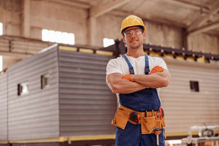 Joyful male builder standing at house building construction site